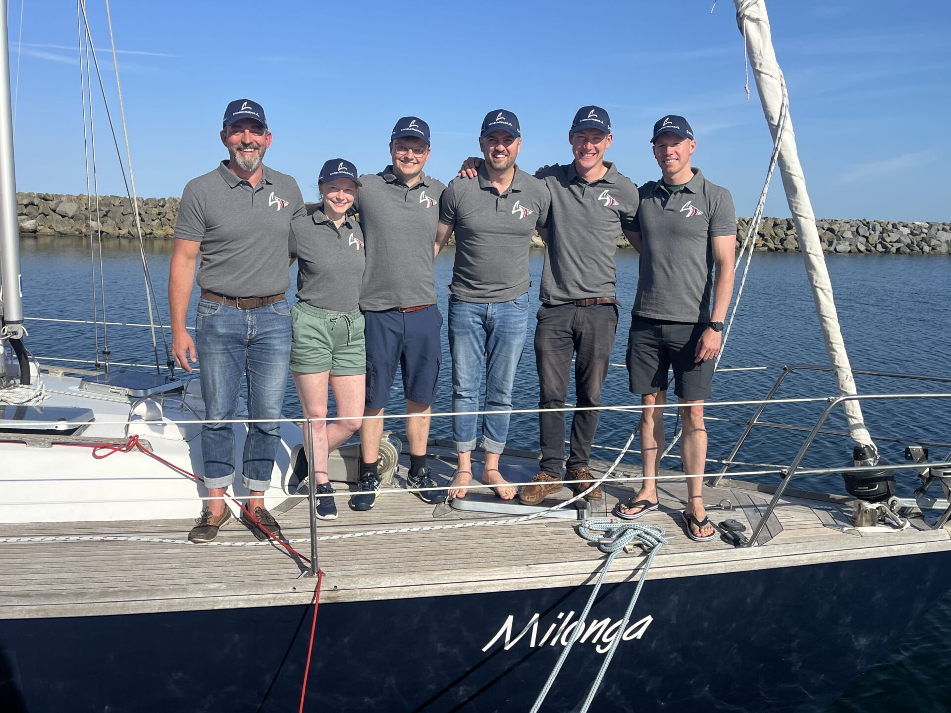 Sechs Personen auf dem Bug der Segelyacht "Milonga" in grauen Polohemden mit dem Logo der MidsummerSail.